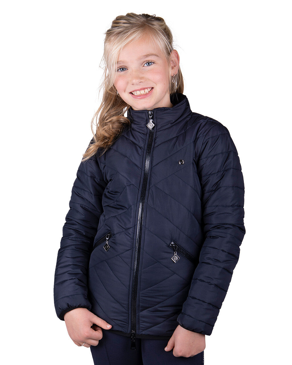 Young girl wearing a navy quilted riding jacket, smiling with hands by her sides, against a plain white background.
